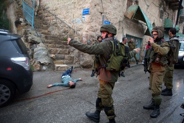 Israeli soldiers stand next to the body of a Palestinian martyr